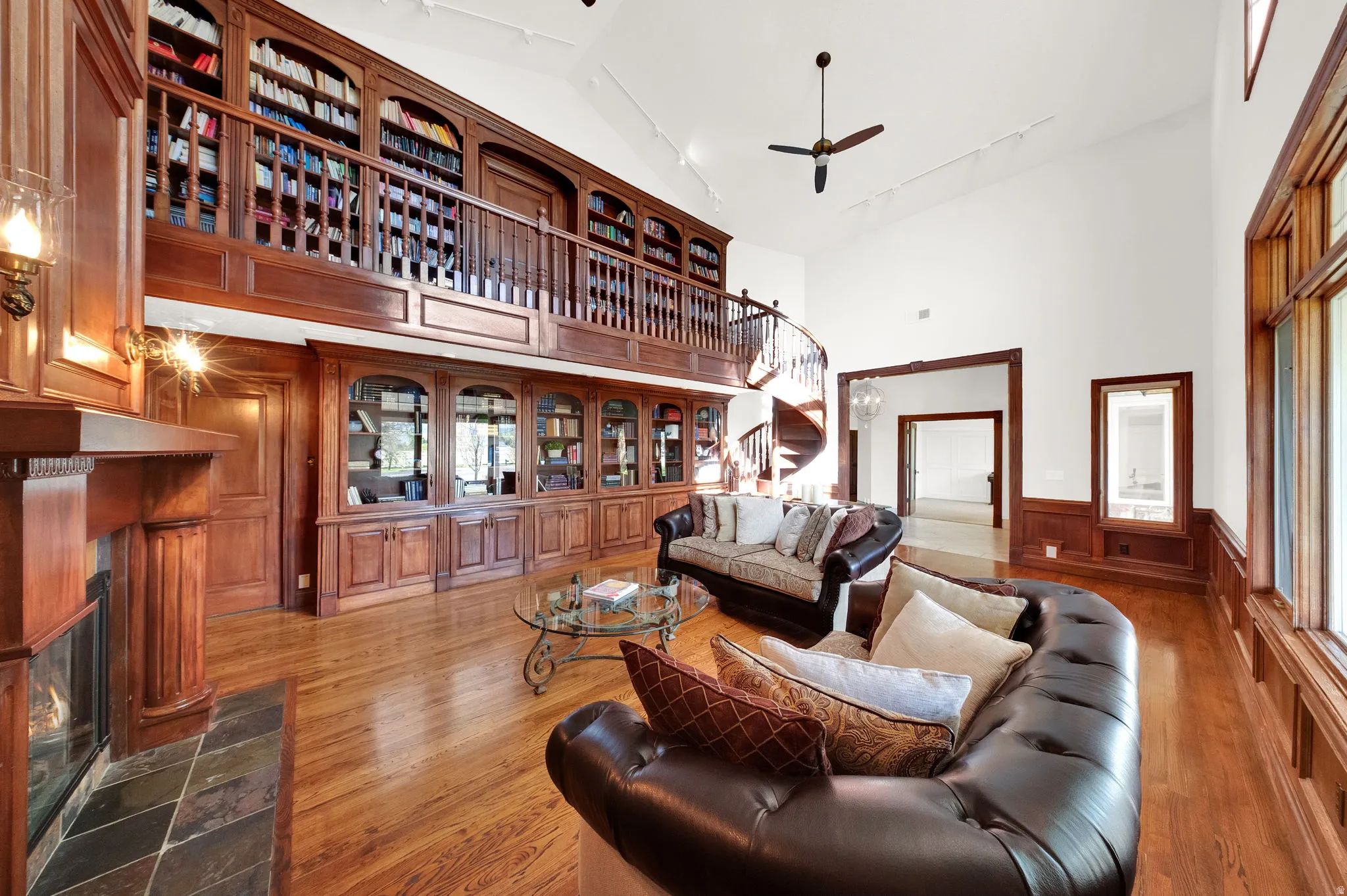 Grand living space featuring a two-story library with built-in shelving, a spiral staircase, and rich wood-finish flooring