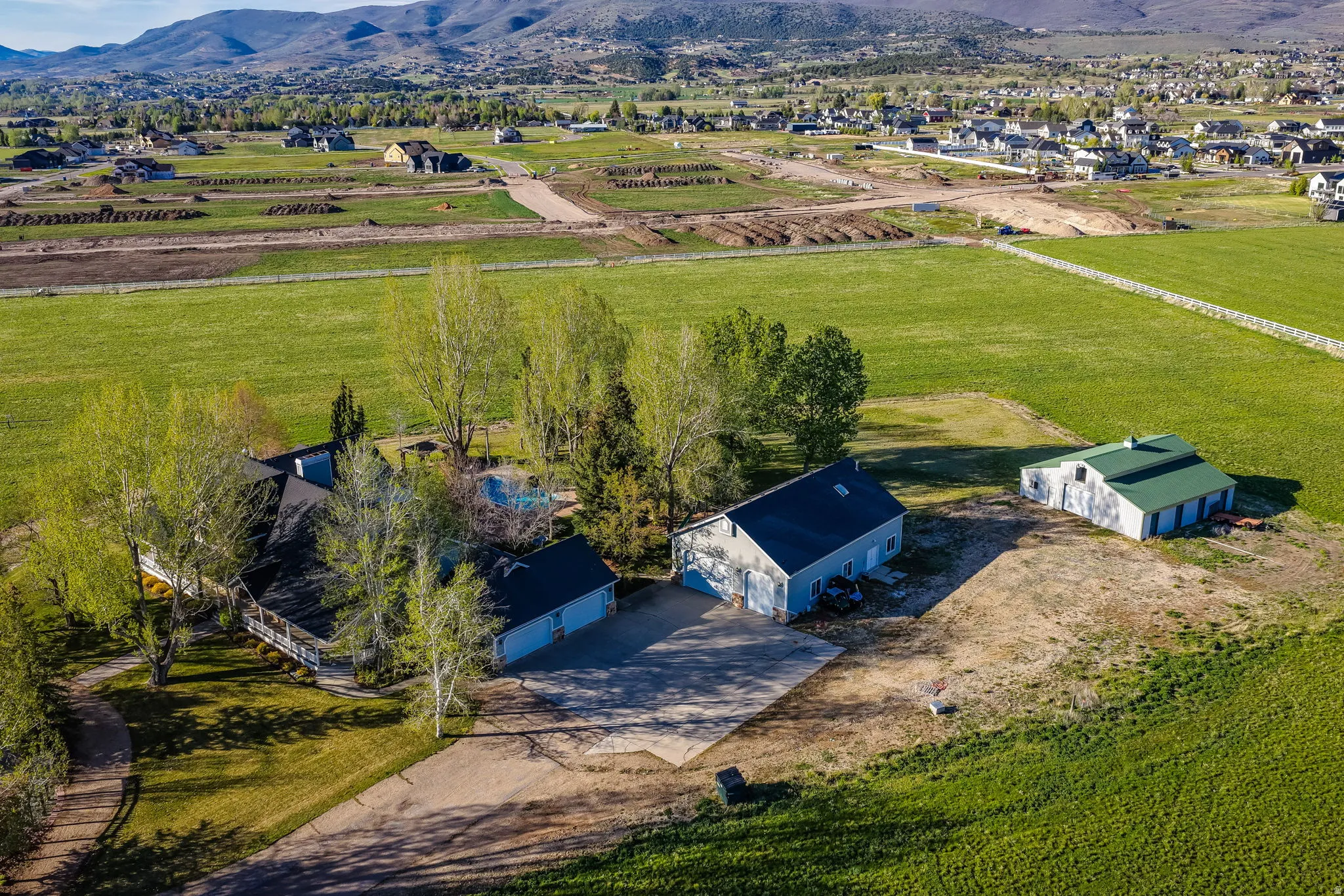 Expansive property featuring a main residence with a large porch, a pool area, and multiple outbuildings, all surrounded by green fields