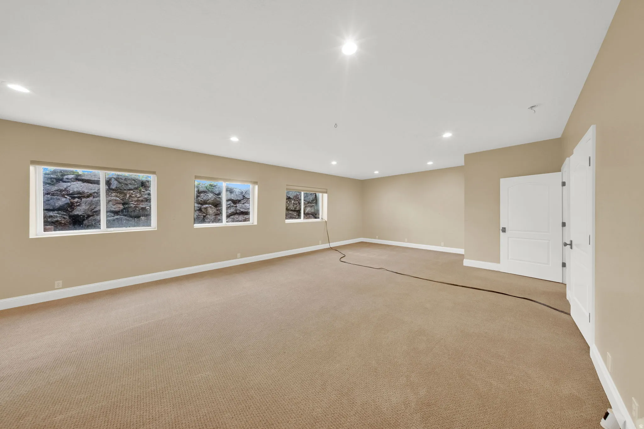 Spacious room featuring neutral wall paint, recessed lighting, white baseboards, and light brown carpet flooring