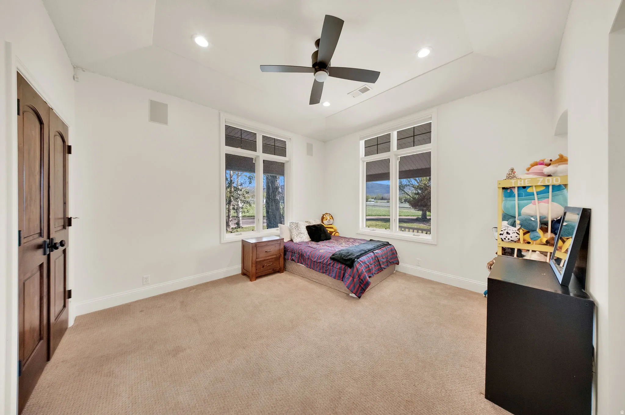 Spacious room featuring broadloom carpeting, two large windows with views of the landscape, a ceiling fan, and recessed lighting
