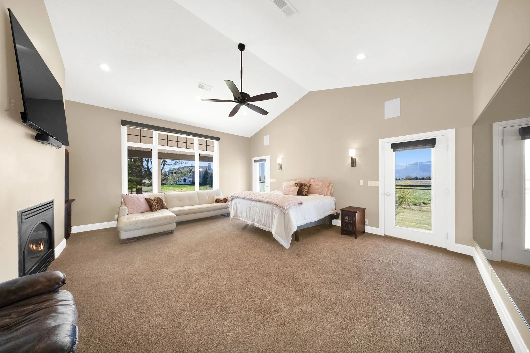 Spacious Primary bedroom featuring vaulted ceilings, a built-in fireplace, expansive windows, and two glass-paneled doors