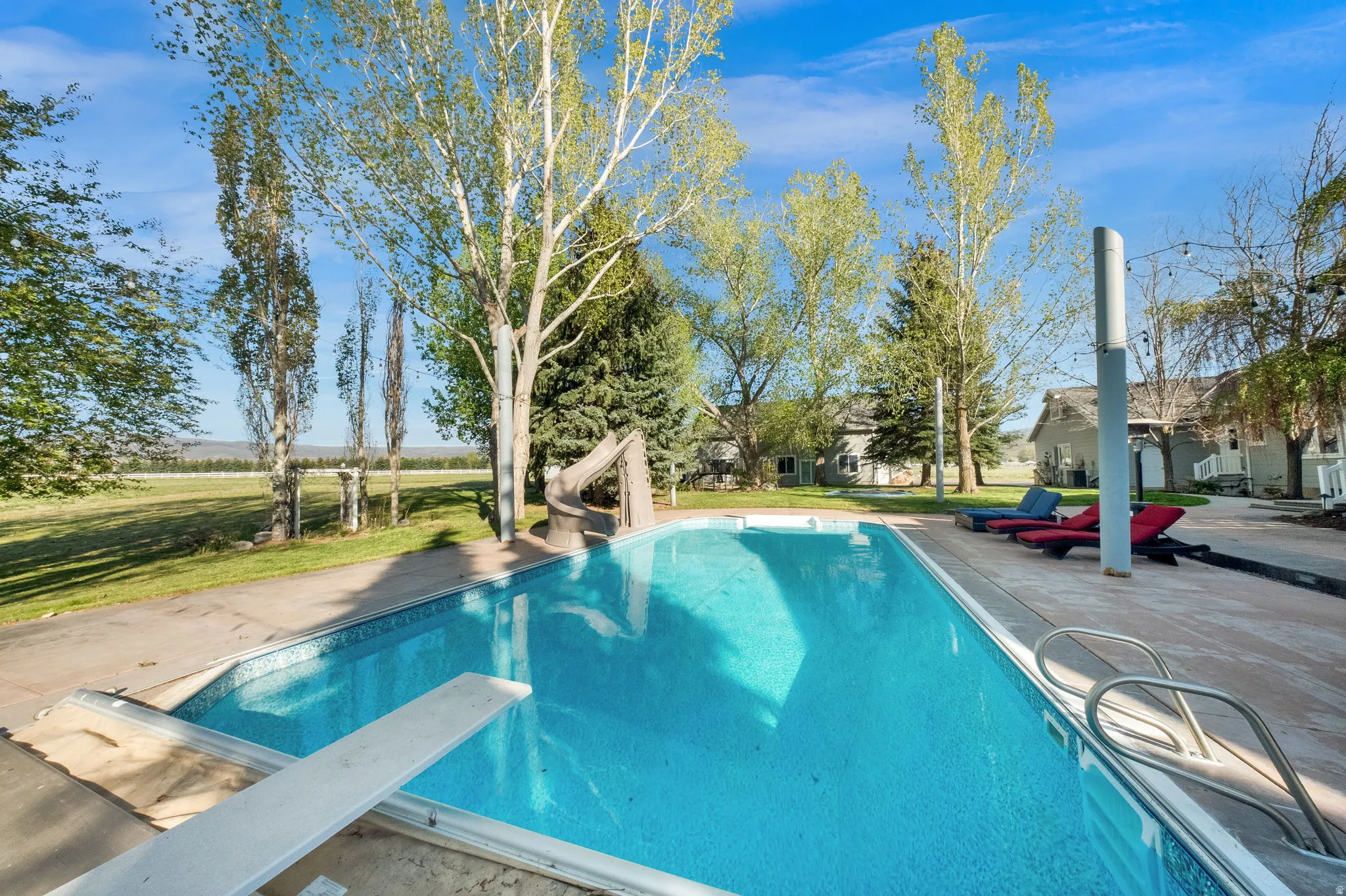 In-ground swimming pool featuring a diving board, water slide, and concrete surround