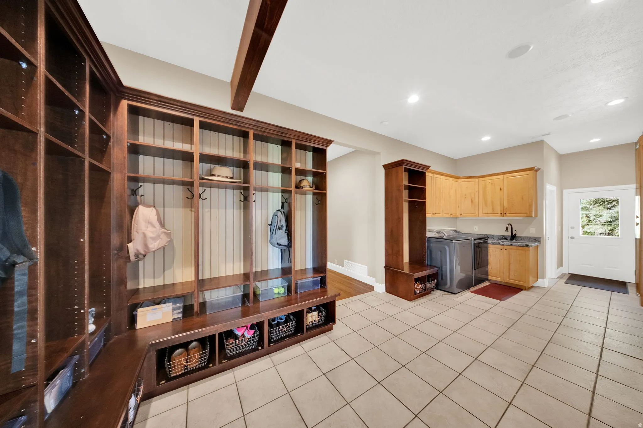 Spacious mudroom featuring extensive built-in wooden cabinetry with individual cubbies and hooks, an integrated bench, and tiled flooring
