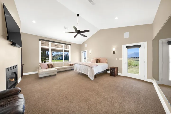 Spacious Primary bedroom featuring vaulted ceilings, a built-in fireplace, expansive windows, and two glass-paneled doors
