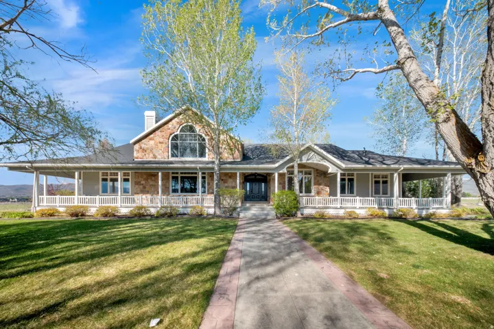 Stone and siding exterior with a large covered wraparound porch, a prominent arched window, a stamped concrete pathway, and mature trees