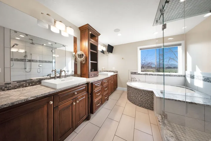 Primary bathroom featuring dual wood-finish vanity with vessel sinks, granite countertops, and full-width mirror