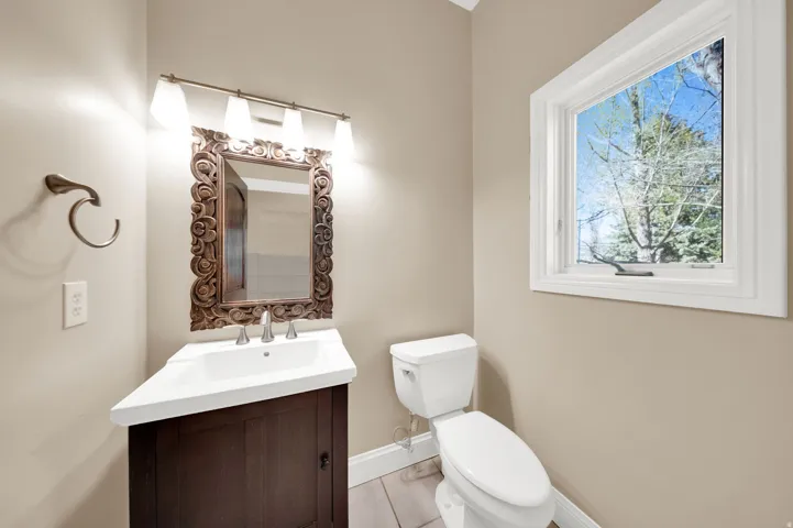 Bathroom featuring a dark wood vanity with white countertop, decorative carved wood-frame mirror, and a window with white trim