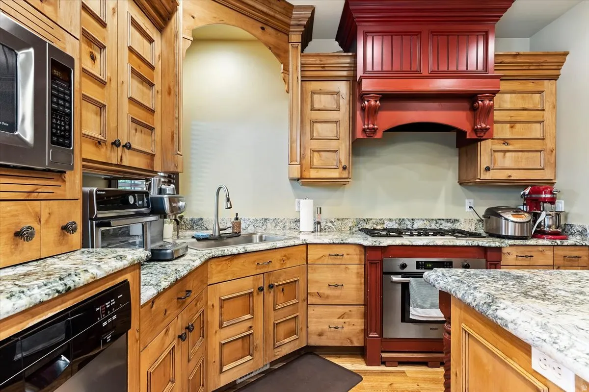 Kitchen featuring wood cabinetry, granite-style countertops, stainless steel appliances, a built-in microwave, and a custom red range hood