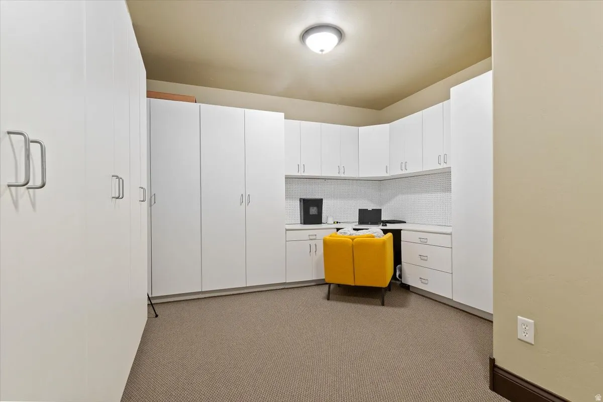 Dedicated office space featuring extensive white cabinetry, a built-in corner desk, and textured carpeting