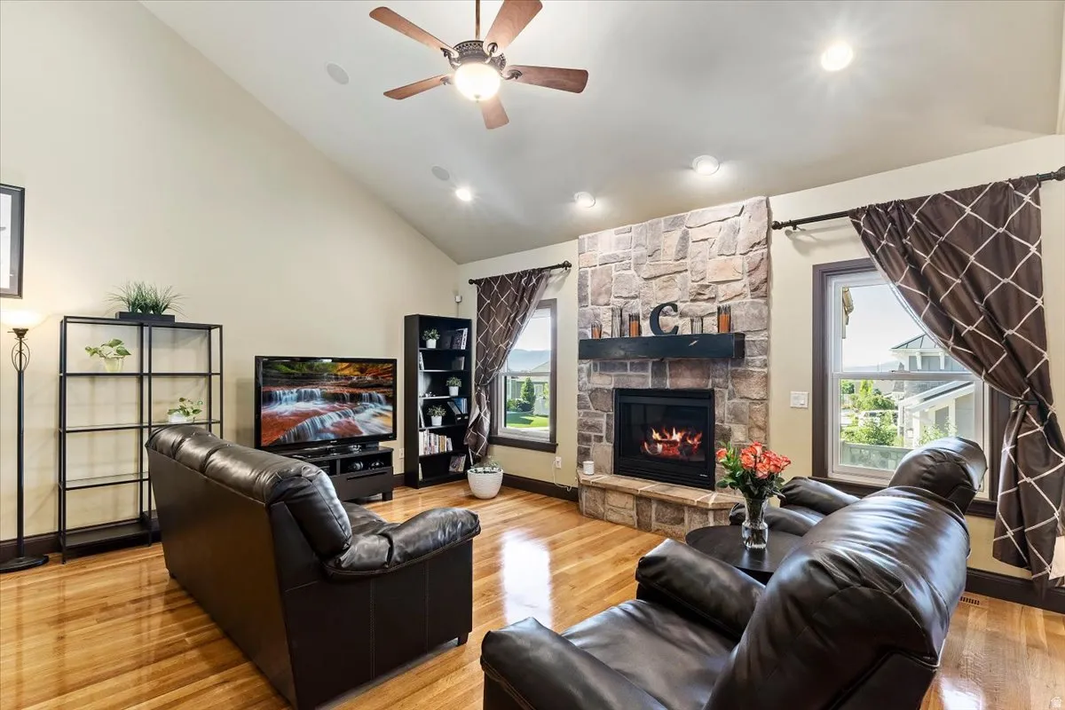 Living area with vaulted ceilings, wood-finish flooring, a stone-surround fireplace with a dark mantel, recessed lighting, and a ceiling fan