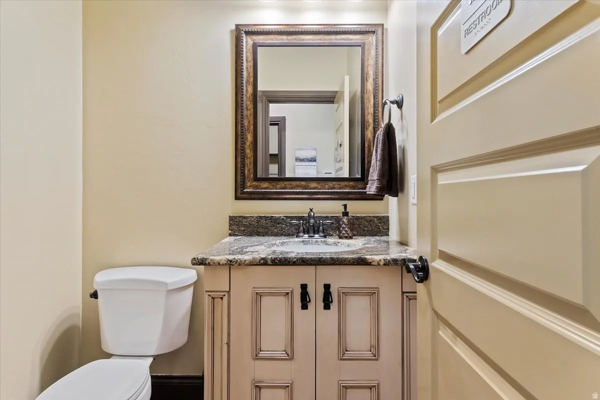 Powder room featuring a custom vanity with a stone countertop, a decorative framed mirror, and a wall-mounted light fixture