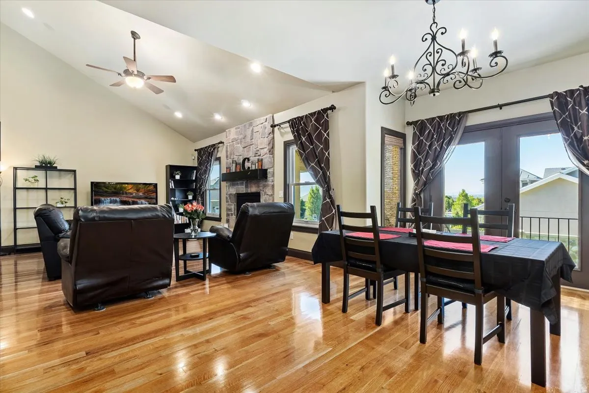 Open-concept living and dining areas featuring wood-finish flooring, a vaulted ceiling, recessed lighting, and a stone-faced fireplace with a dark wood mantel