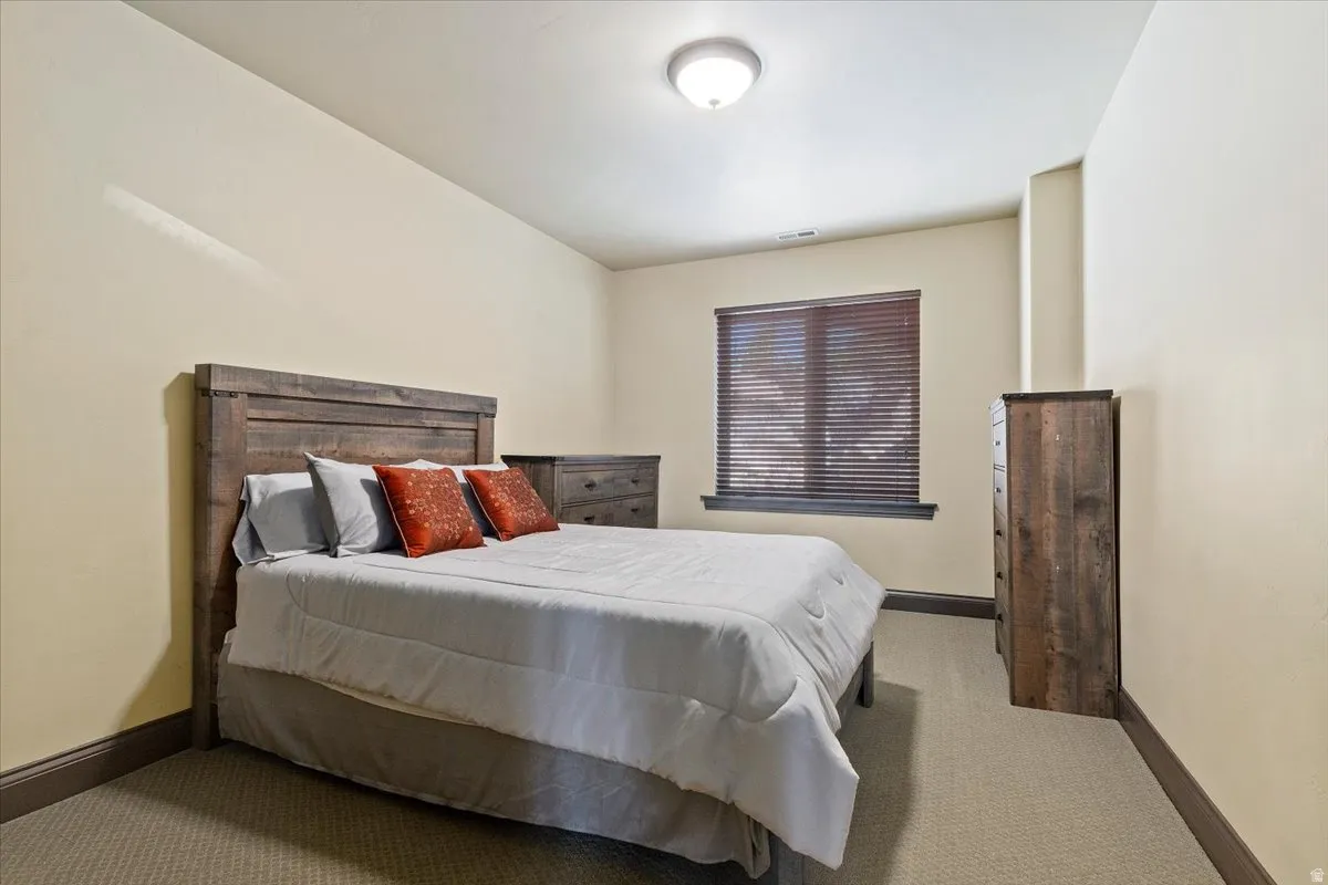 Spacious room featuring neutral carpeting, light-toned walls, a single window with dark wood blinds, recessed lighting, and dark baseboards