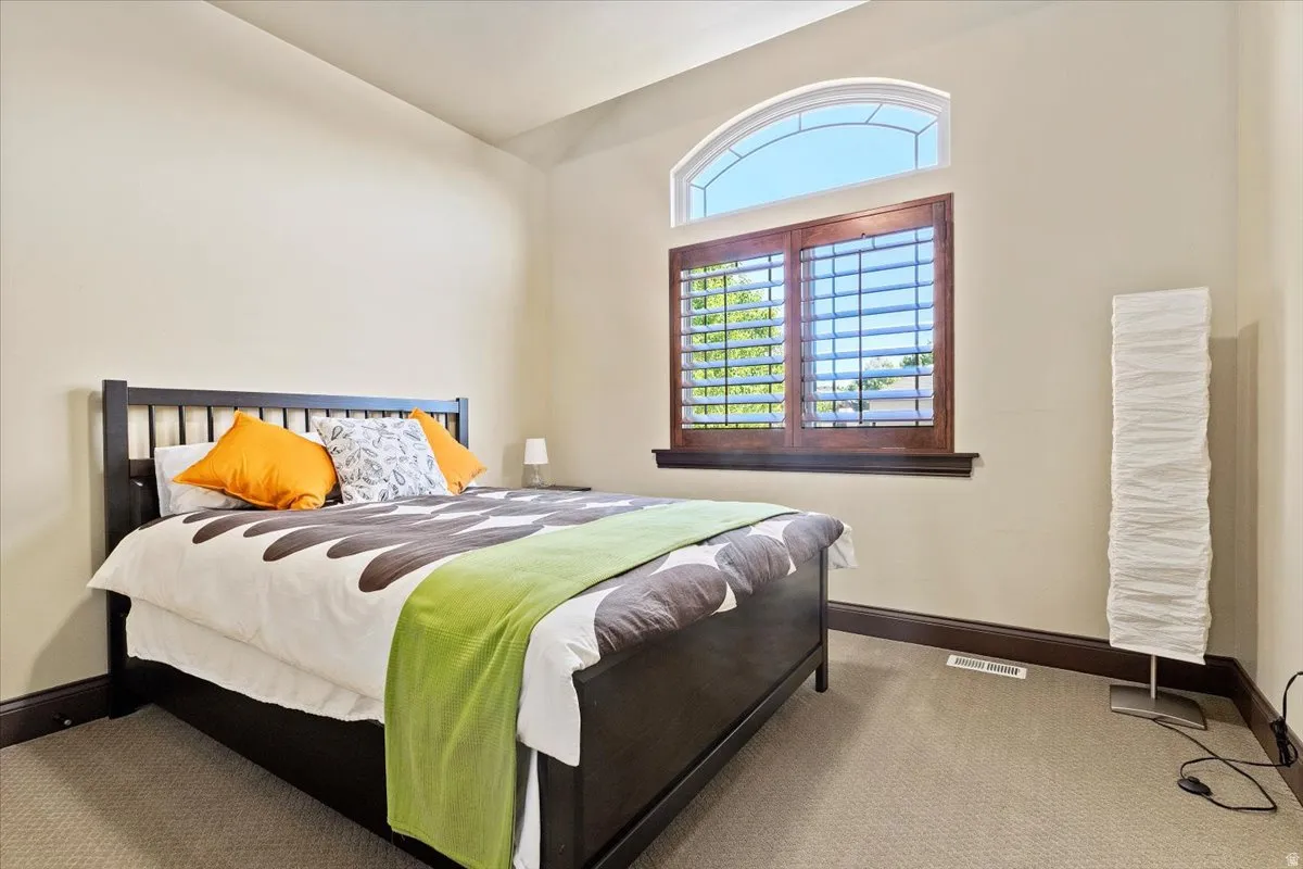 Carpeted room featuring a large arched window with decorative muntins, complemented by wood-finish plantation shutters