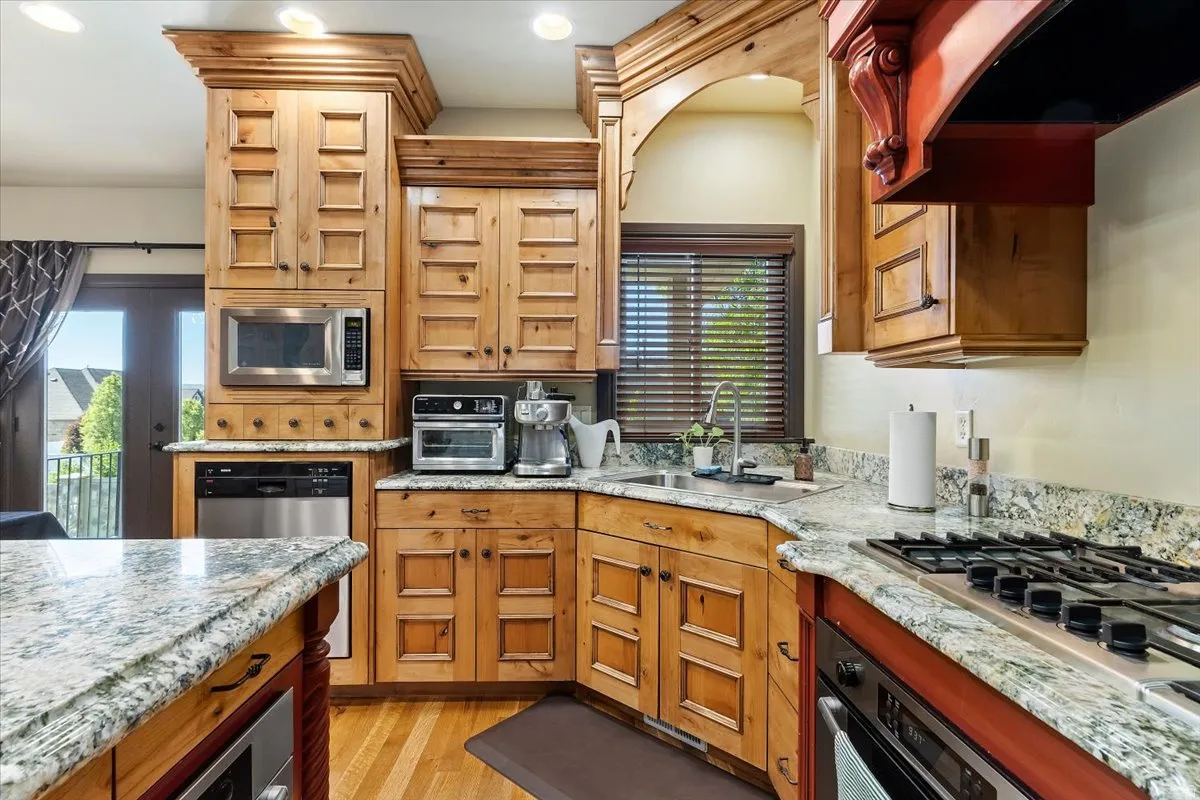 Kitchen featuring light wood cabinetry with decorative molding, granite countertops, stainless steel appliances, a built-in microwave, and wood-finish flooring