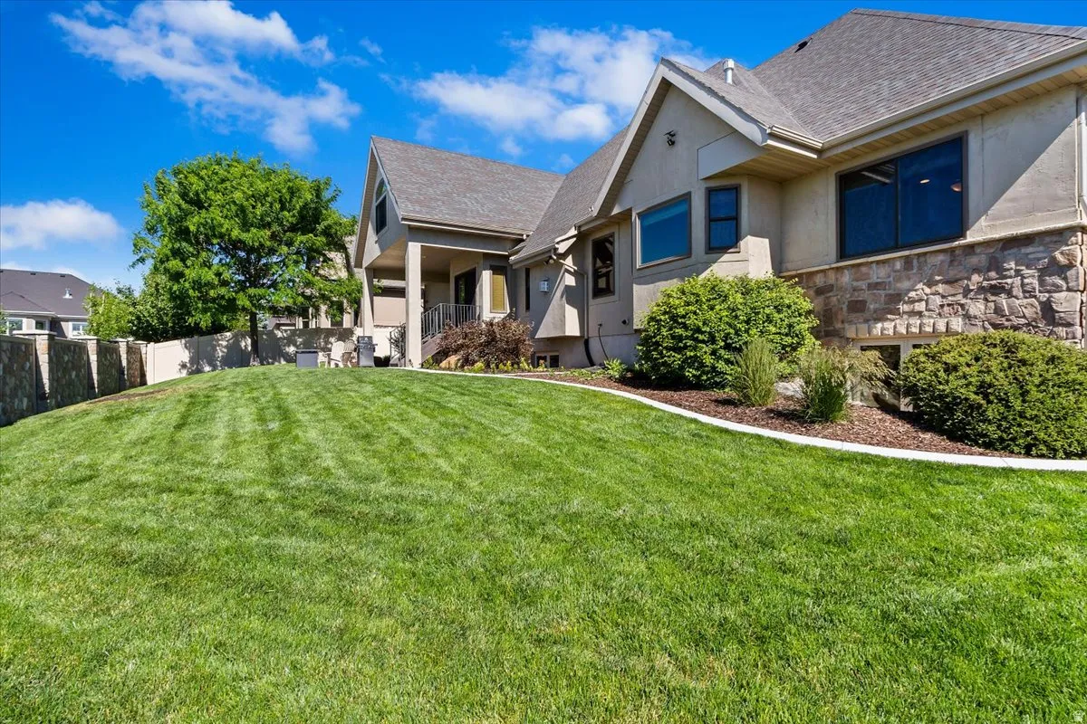 Expansive green lawn sloping towards a multi-level home featuring stucco siding, stone accents, and a grey shingle roof