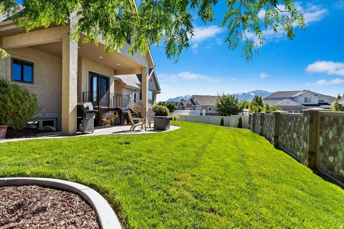 Spacious lawn featuring a stone and stucco privacy wall, a concrete patio, and mature landscaping
