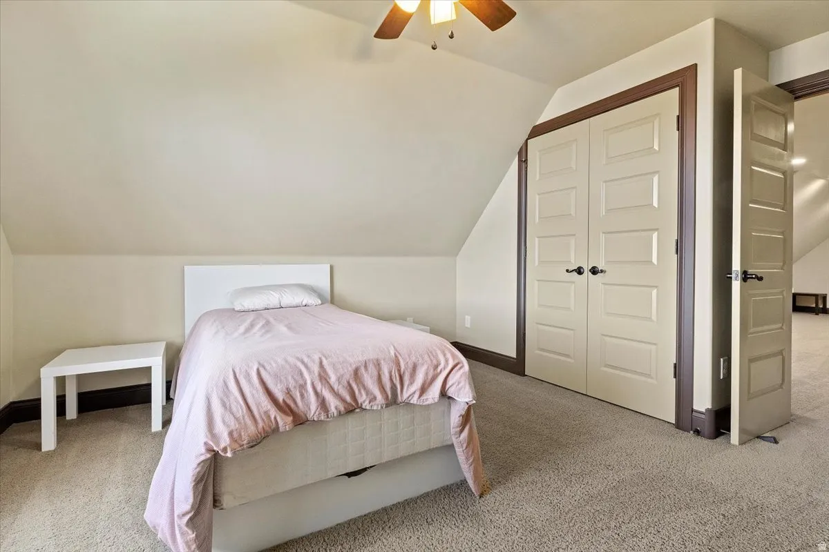 Carpeted room with a ceiling fan, featuring a sloped ceiling and light-toned walls