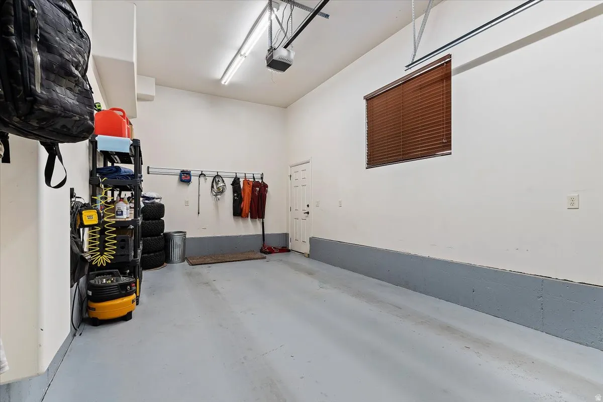 Spacious garage featuring a durable light gray floor, white walls with a contrasting gray kick plate, and a window with wood-finish blinds