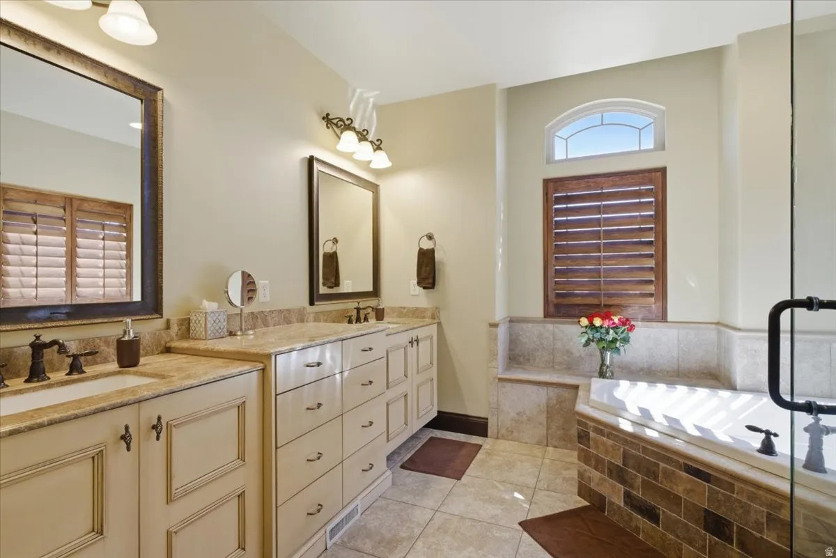 Tiled bathroom featuring a built-in soaking tub, a separate glass-enclosed shower, and a double vanity with integrated sinks