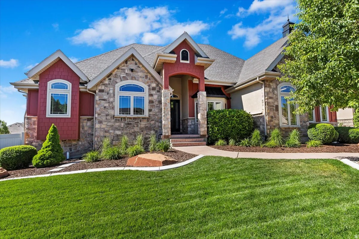 Stone and siding exterior with arched entry, complementing arched windows, and a mature landscaped front yard with a concrete pathway