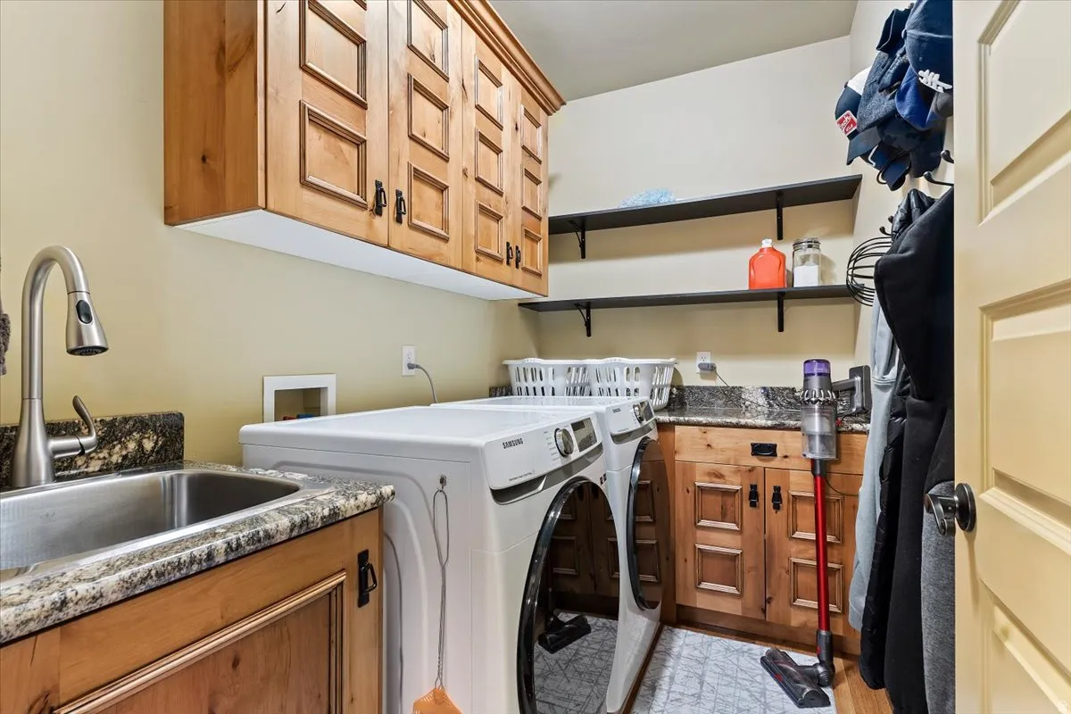 Utility room featuring wood cabinetry, stone countertops, a stainless steel sink with a gooseneck faucet, and open shelving