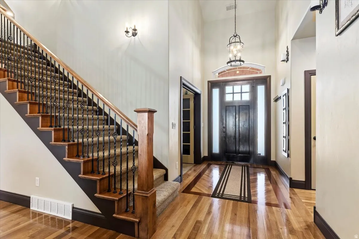 Grand entryway featuring a double door with glass accents, hardwood flooring with decorative inlay, and a wrought iron chandelier