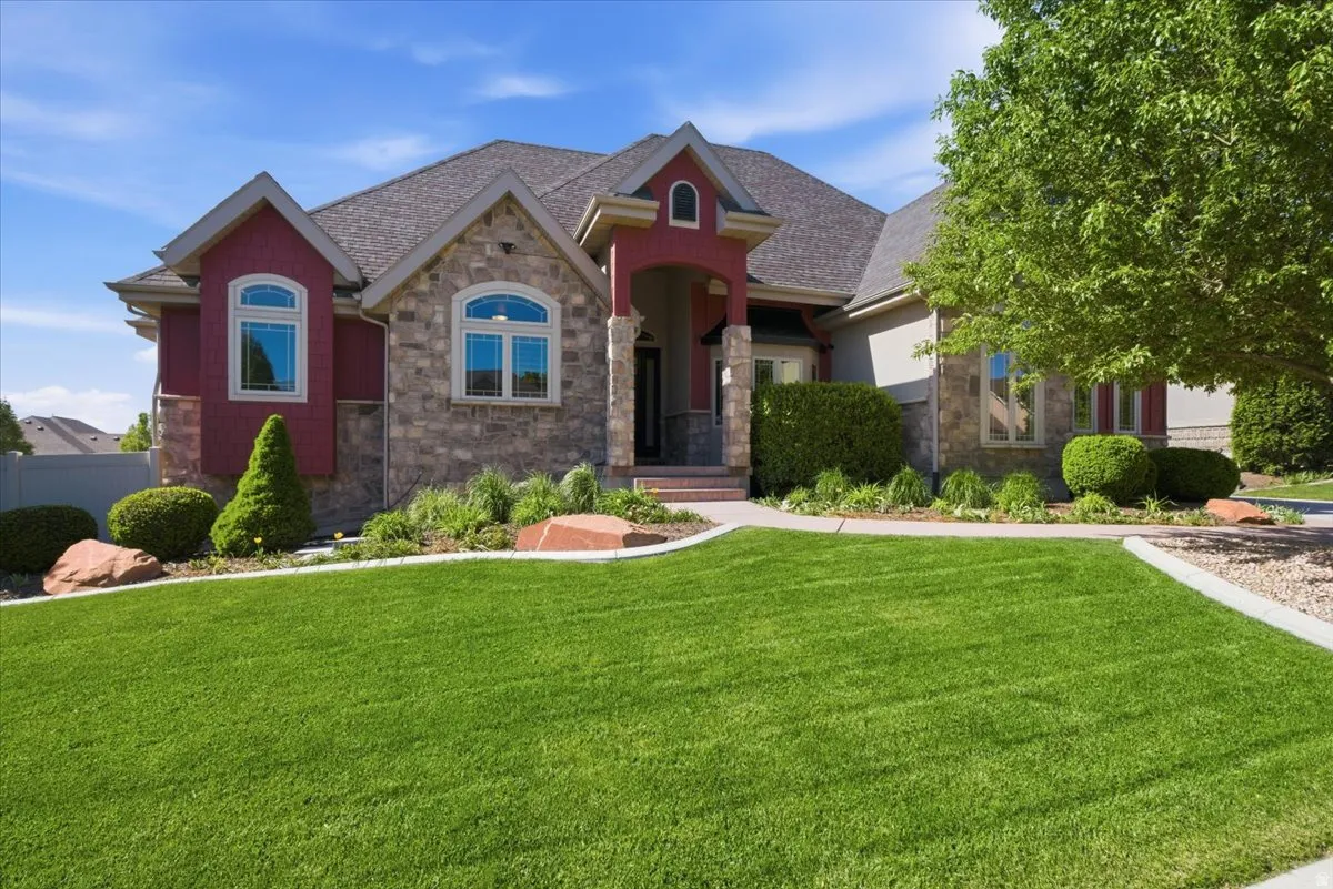 Stone and siding exterior with arched windows, a covered entry, and a manicured lawn