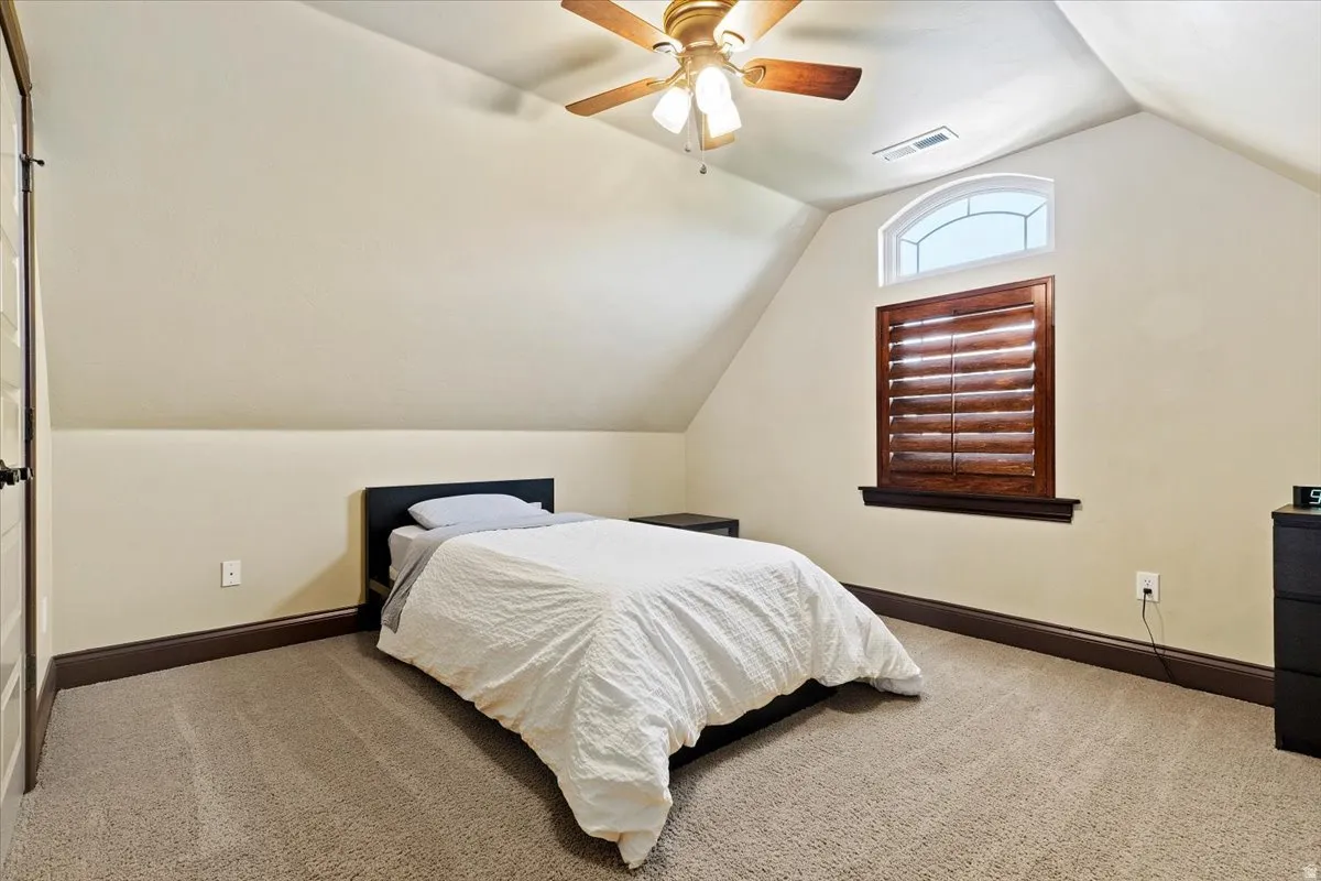 Carpeted room featuring a ceiling fan with integrated lighting, a wooden plantation shutter window treatment, and a transom window