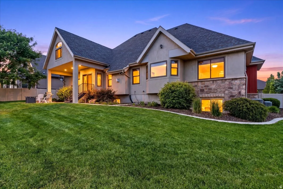 Rear exterior featuring a covered patio, extensive lawn, and a facade with stone accents