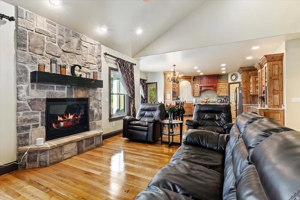 Living area featuring a stone-clad fireplace with a dark wood mantel, wood-finish flooring, and a vaulted ceiling