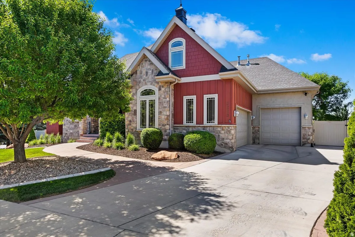 Stone and red siding exterior featuring an arched window, a two-car garage, manicured landscaping, and a paved driveway