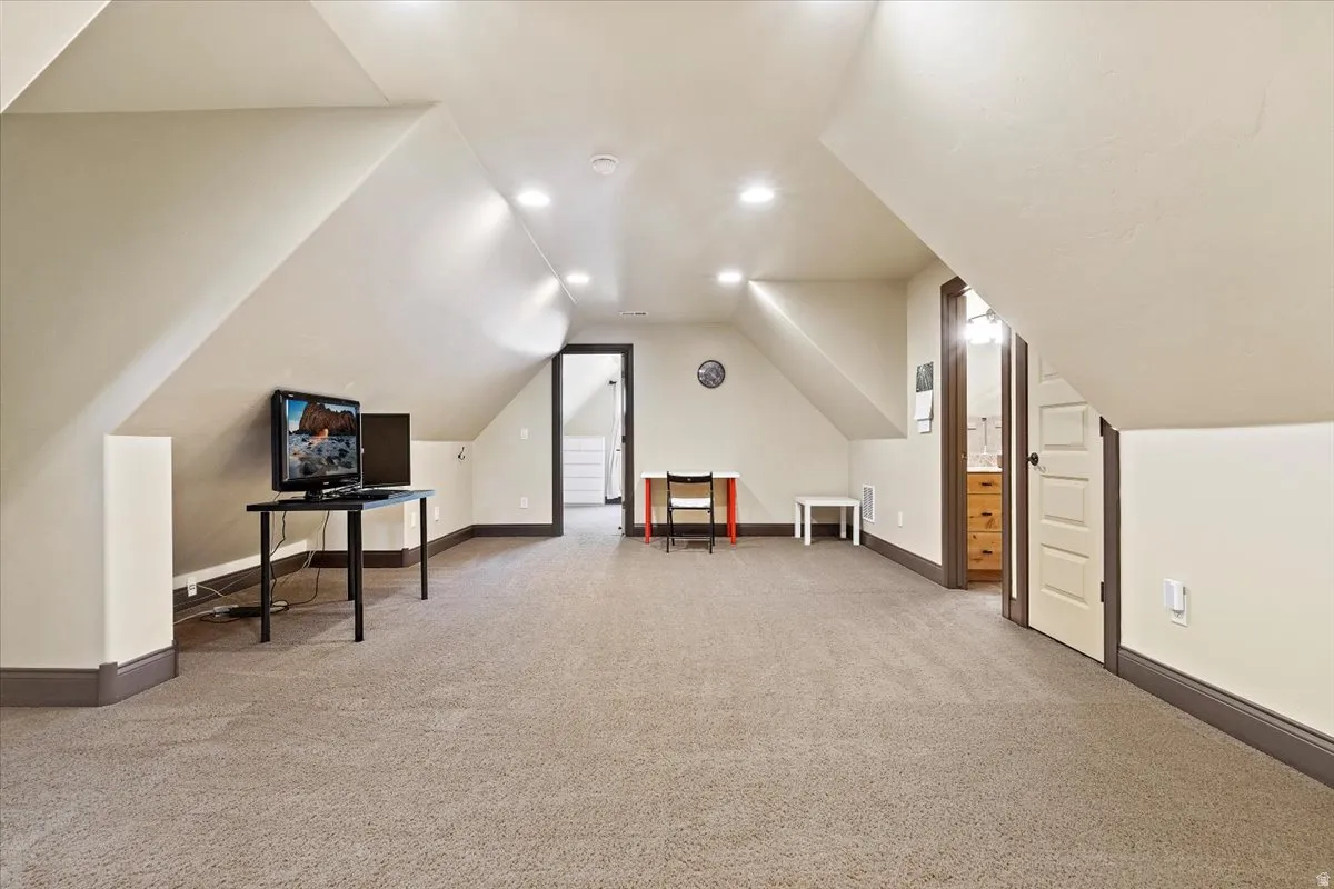 Carpeted bonus room featuring sloped ceilings, recessed lighting, neutral wall paint, and dark-stained trim work