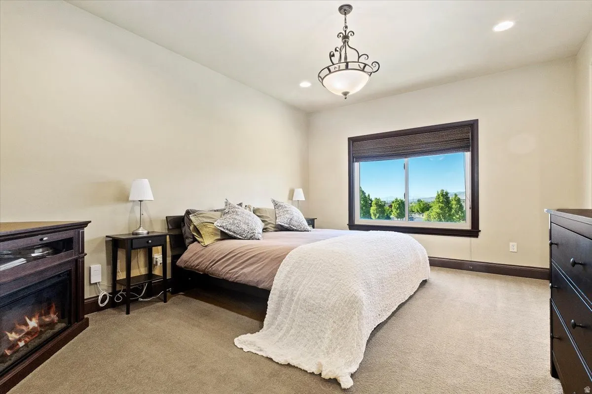 Bedroom with warm neutral walls, carpeted flooring, a large window with dark trim, and a built-in electric fireplace