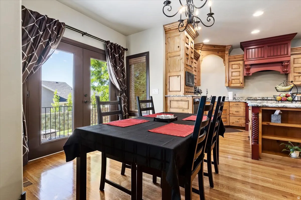 Hardwood flooring extends through the dining area and kitchen, featuring French doors with a balcony, custom wood cabinetry, granite countertops, and a decorative range hood