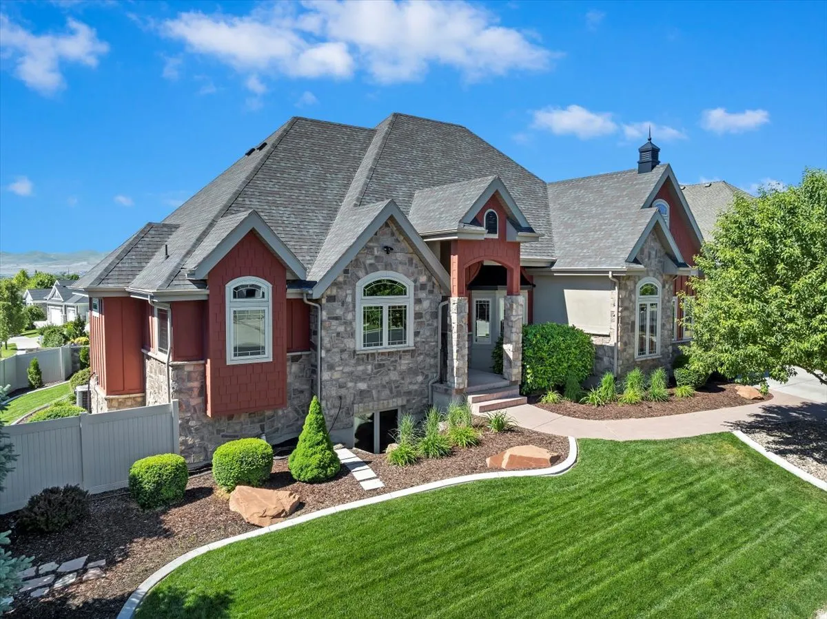 Stone and siding exterior with a multi-level roofline, featuring an arched entry and a landscaped front yard with a curved walkway