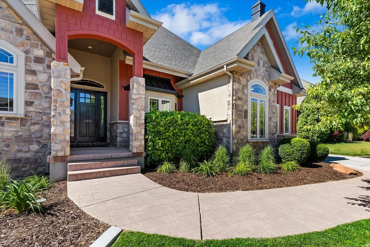 Stone and siding exterior with architectural detailing, featuring a covered entry, arched front door, and a curved concrete pathway