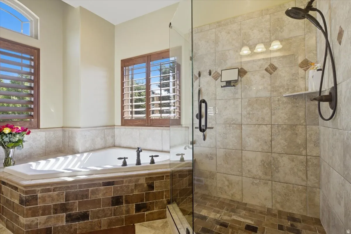 Soaking tub with bronze fixtures, framed by plantation shutters and a high arched window