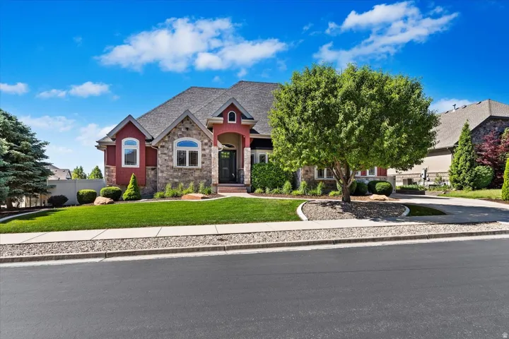 Exterior featuring red siding, stone accents, arched windows, a covered entry, and a paved driveway
