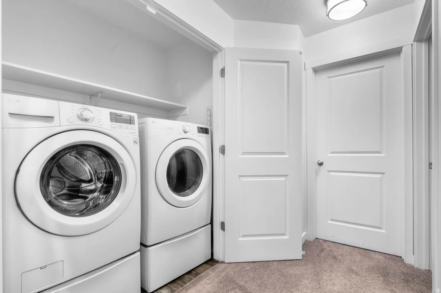 Dedicated laundry area featuring a front-loading washer and dryer, integrated pedestals, and convenient shelving