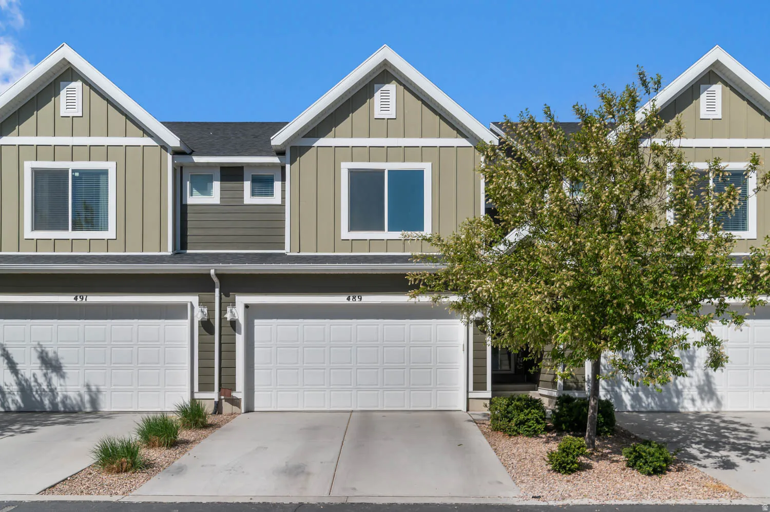 Townhome exterior featuring board and batten siding with white trim, a dark shingle roof, and attached garages