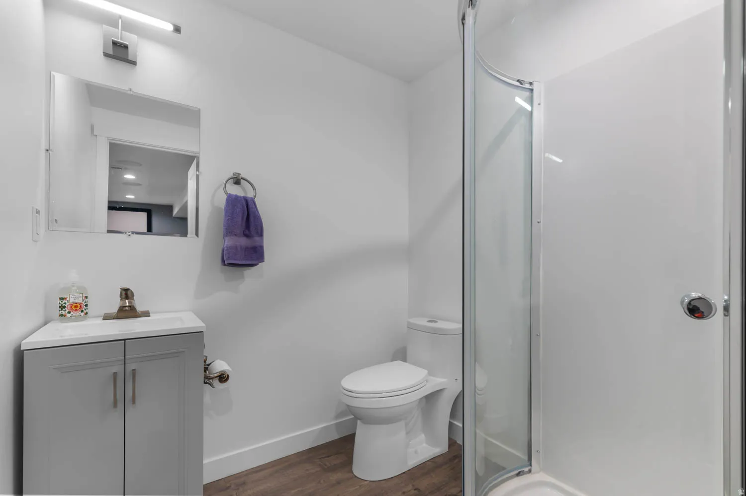 Bathroom featuring a corner vanity with a light gray cabinet and white countertop, a contemporary toilet, and a glass-enclosed shower stall