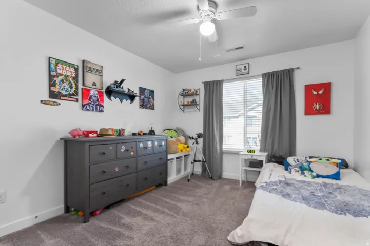 Carpeted room featuring a white ceiling fan with integrated lighting, a large window with blinds and dark-toned drapes, and white baseboards