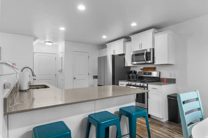 Kitchen featuring an expansive counter-height island with a sink, white cabinetry, stainless steel appliances, recessed lighting, and wood-finish flooring