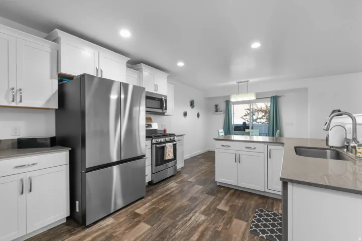 Bright kitchen featuring white shaker cabinetry, stainless steel appliances, wood-finish flooring, recessed lighting, and light-toned countertops
