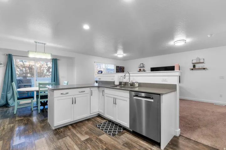 Contemporary kitchen featuring white cabinetry, a stainless steel dishwasher, a single basin sink with a high-arc faucet, and light gray countertops