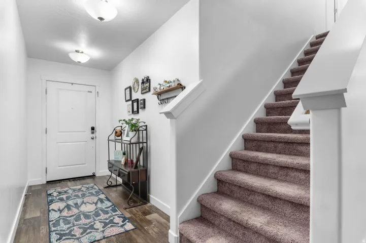 Inviting entryway featuring wood-finish flooring, a white paneled door, and a carpeted staircase with white trim
