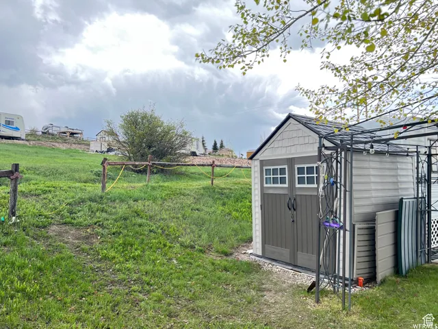 Detached storage shed featuring dual entry doors with windows, shingle-style siding, and a gabled roofline