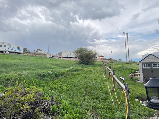 Expansive grassy terrain with a partial split-rail fence and an outdoor storage shed