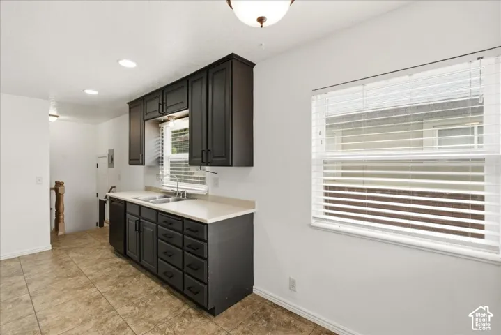 Kitchen featuring dark cabinetry, light countertops, dual basin sink with a window above, and tiled flooring